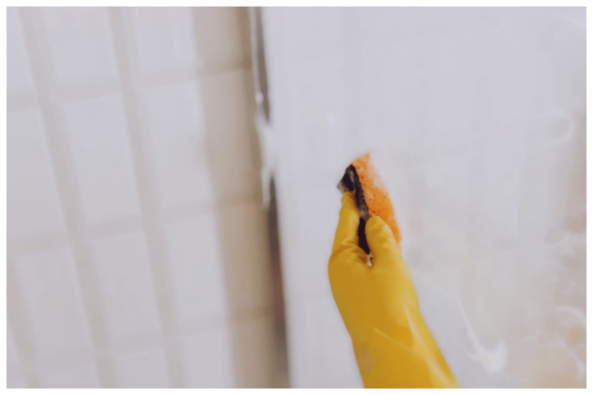 Pessoa usando de borracha amarela pressionando um borrifador para aplicar removedor de manchas no box de vidro do banheiro